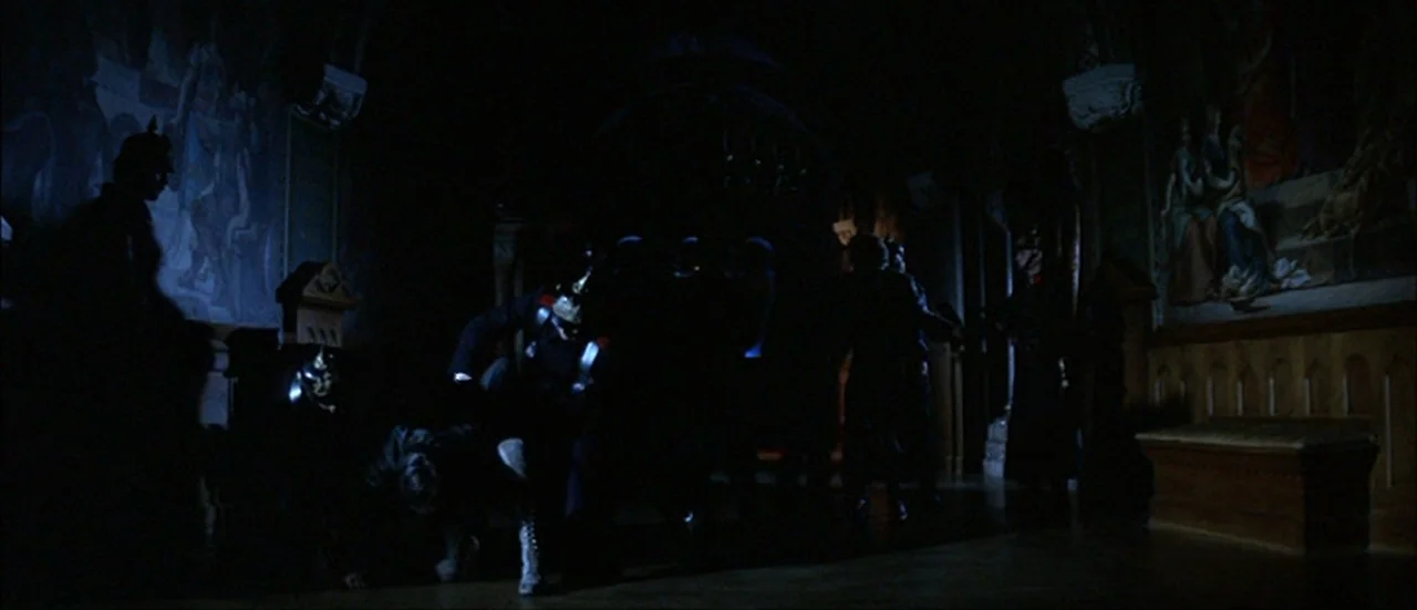 Ludwig (1973) movie still: wide — A dimly lit corridor features dark wood paneling and large wall paintings. Several figures in dark military…
