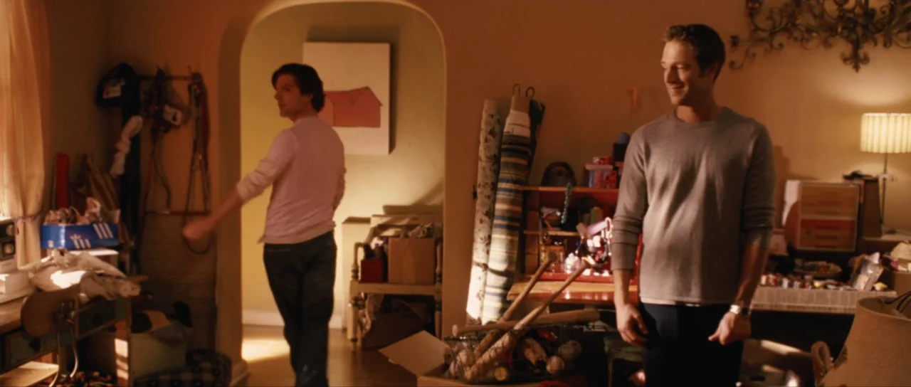 Monster-in-Law (2005) movie still: medium — A cluttered craft room contains fabric rolls, boxes, and miscellaneous storage items. One man stands in…