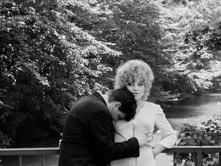Katzelmacher (1969) movie still: medium — A man and woman stand on a bridge overlooking a river surrounded by dense trees. The man leans his head…