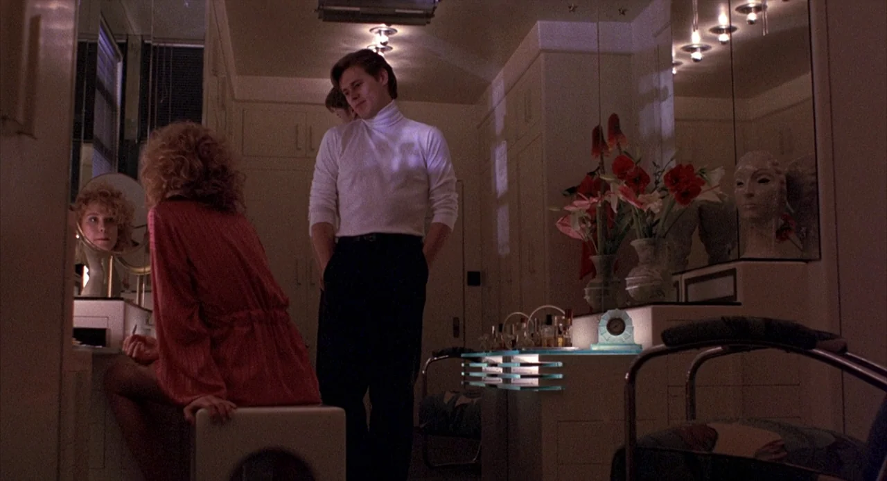 To Live and Die in L.A. (1985) movie still: medium — A well-appointed, dimly lit dressing room features mirrored walls and a vanity area. A man in a…