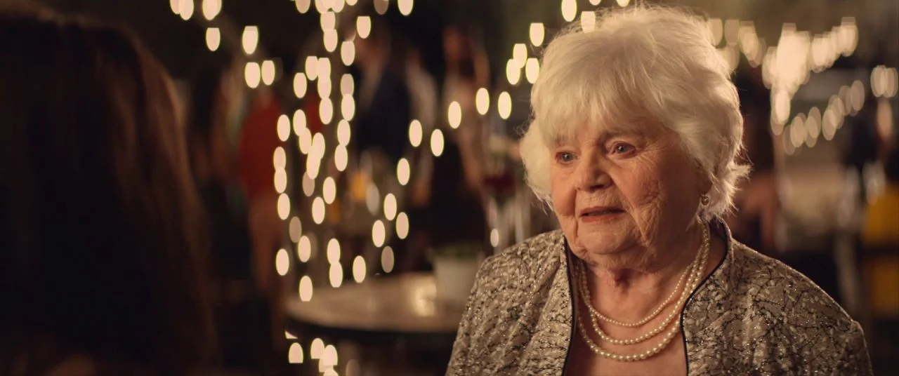 Palm Springs (2020) movie still: closeup — An outdoor evening gathering features blurred bokeh string lights creating a festive background effect.…