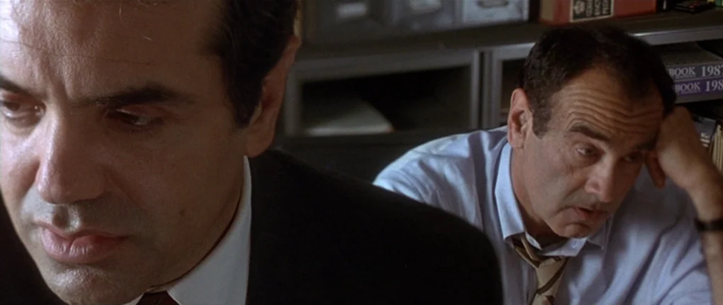 The Usual Suspects movie still: Two men sit in a cramped office, both lost in a moment of exhaustion or quiet despair. The lack of interaction and…