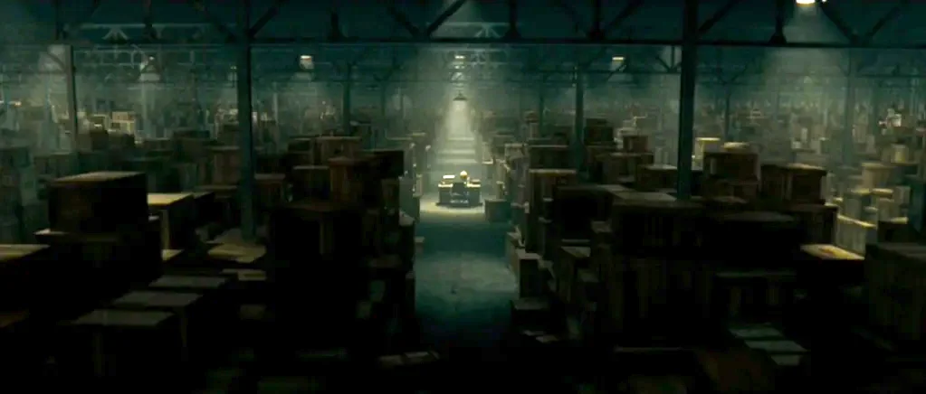 Paul (2011) movie still: establishing — A massive, dimly lit storage facility is filled with endless rows of wooden crates. A single desk sits…