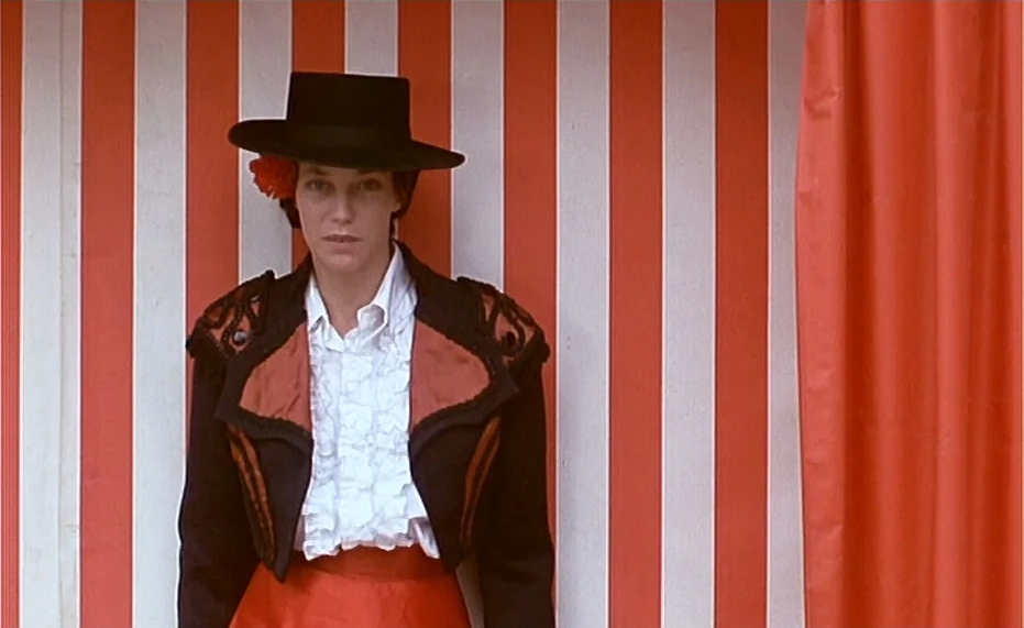 Jane B. par Agnès V. (1988) movie still: medium — A person stands against a backdrop of vertical red and white striped canvas. The individual wears…