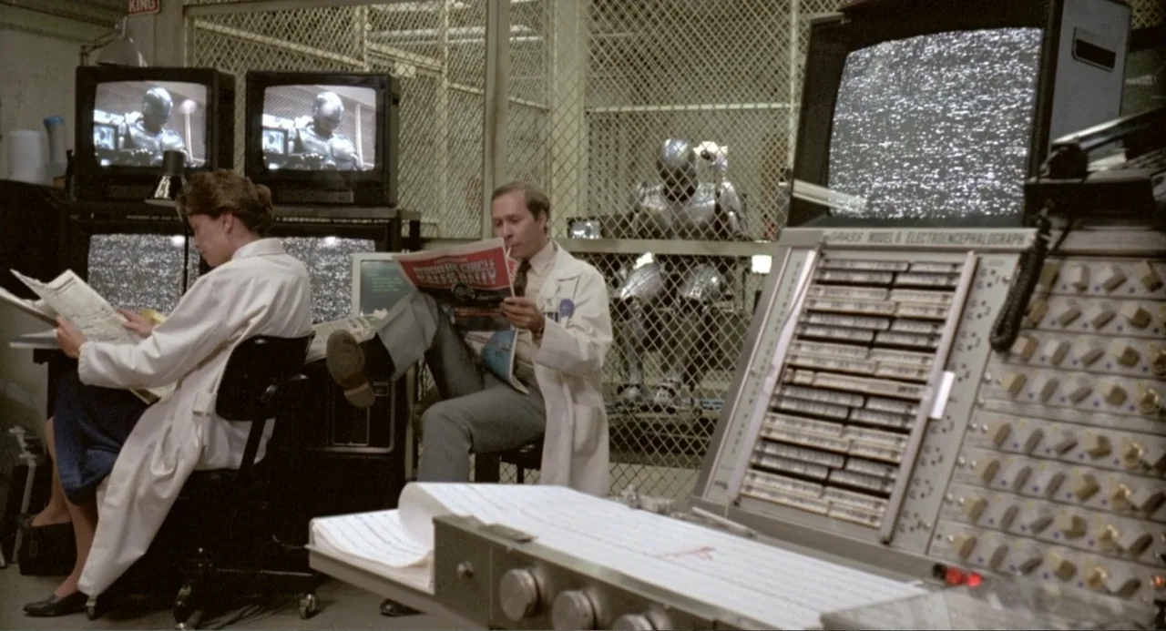 RoboCop (2014) movie still: medium — A laboratory features caged partitions and multiple television monitors displaying static or robotic imagery.…