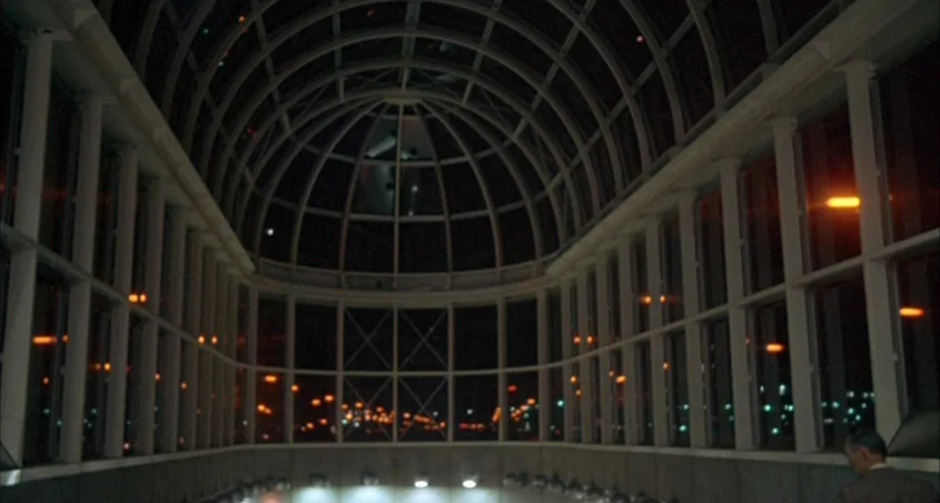 Scanners (1981) movie still: wide — A spacious architectural atrium features a high barrel-vaulted glass ceiling and gridded wall panels. Rows of…