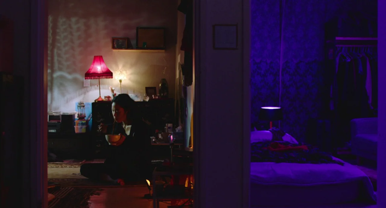 Return To Seoul (2022) movie still: medium — An apartment is viewed through a doorway, showing two rooms with distinct color schemes. A young woman…