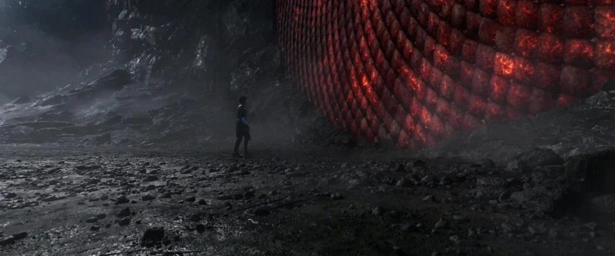 Shang-Chi and the Legend of the Ten Rings (2021) movie still: wide — A dark rocky volcanic expanse features a towering red scaled wall of a…