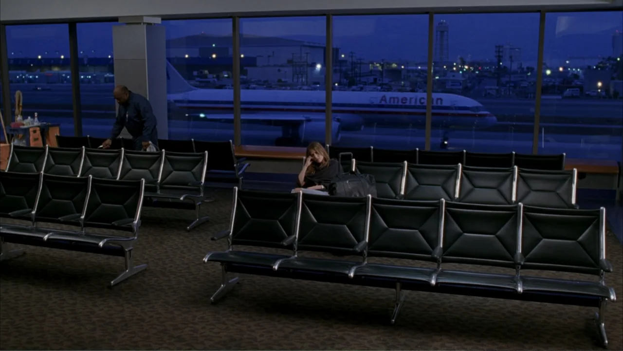 Rumor Has It... (2005) movie still: wide — An empty airport terminal at night features rows of black plastic seats before windows. A lone woman…