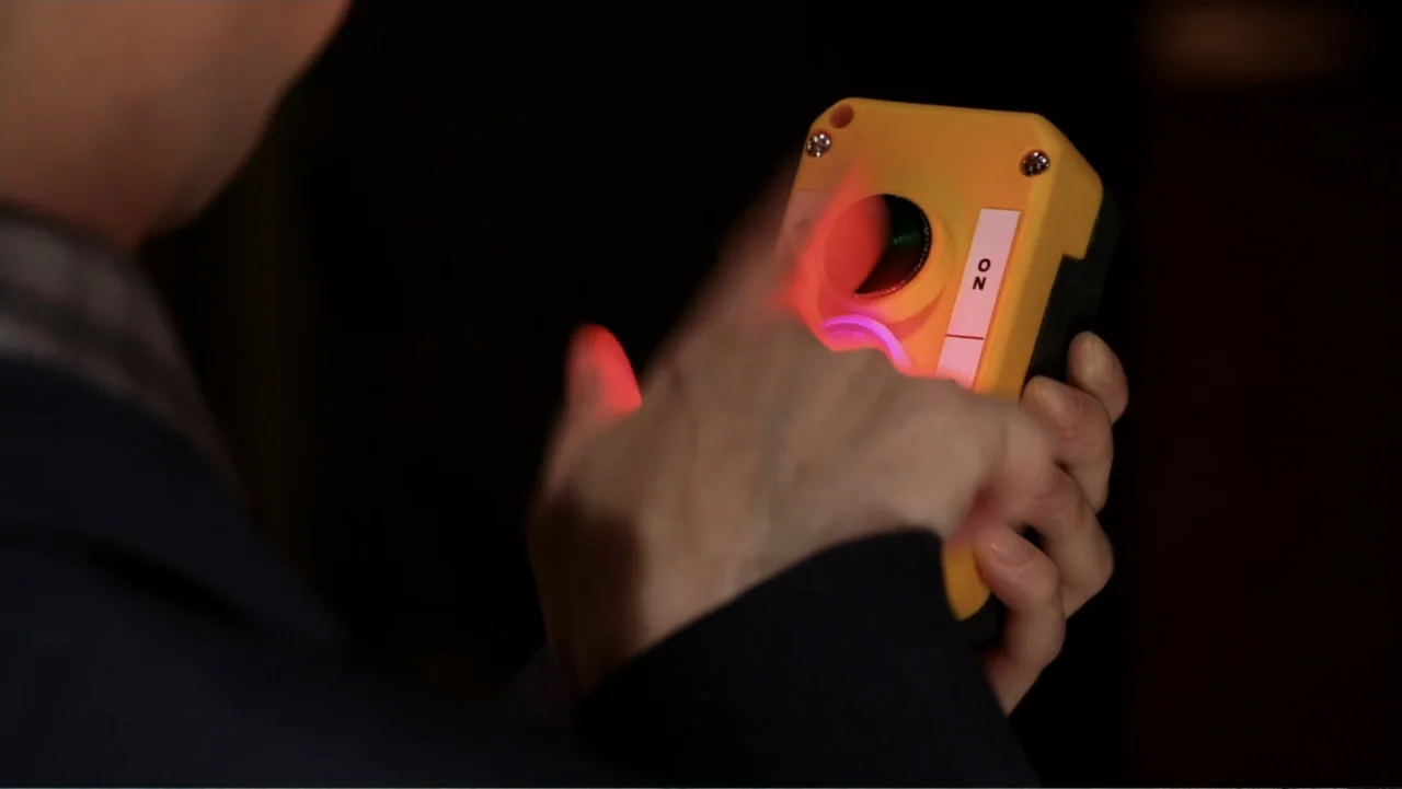 Rufus 2 (2017) movie still: closeup — A dark industrial environment contains a person holding a yellow industrial control box. A person operates the…