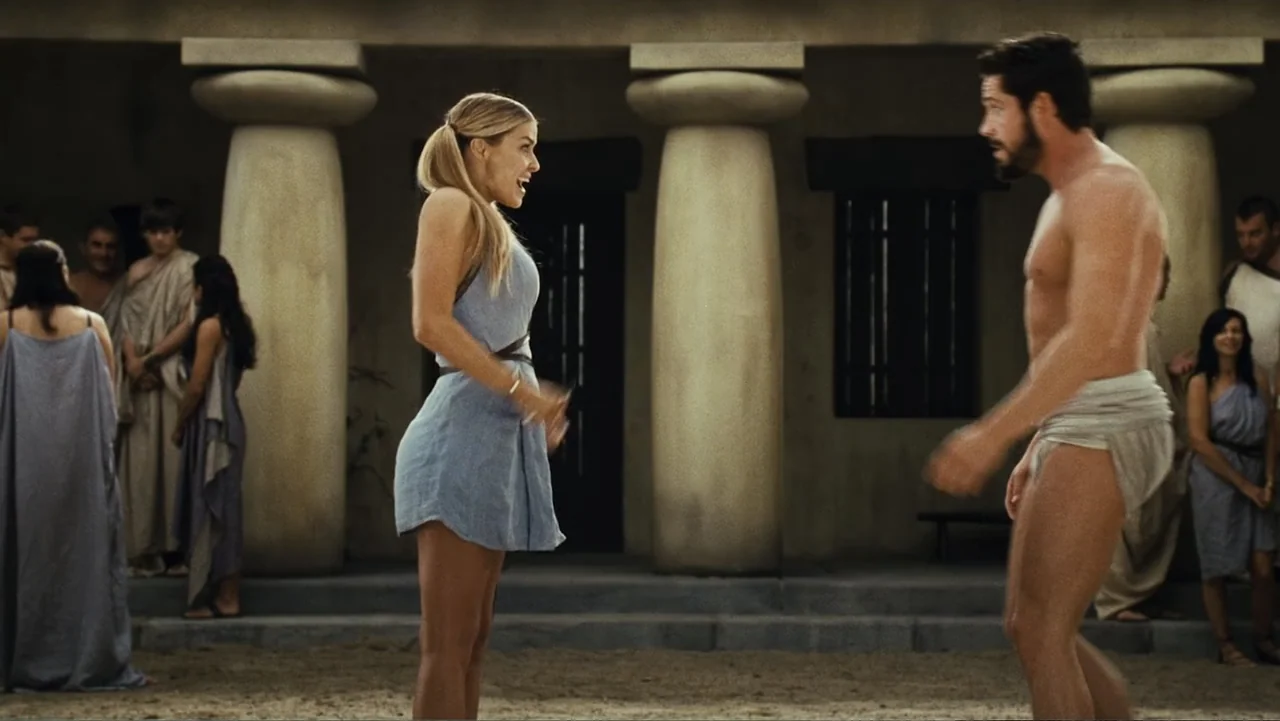 Meet the Spartans (2008) movie still: fullbody — A classical stone portico with large round pillars stands against a sandy ground. A blonde woman…