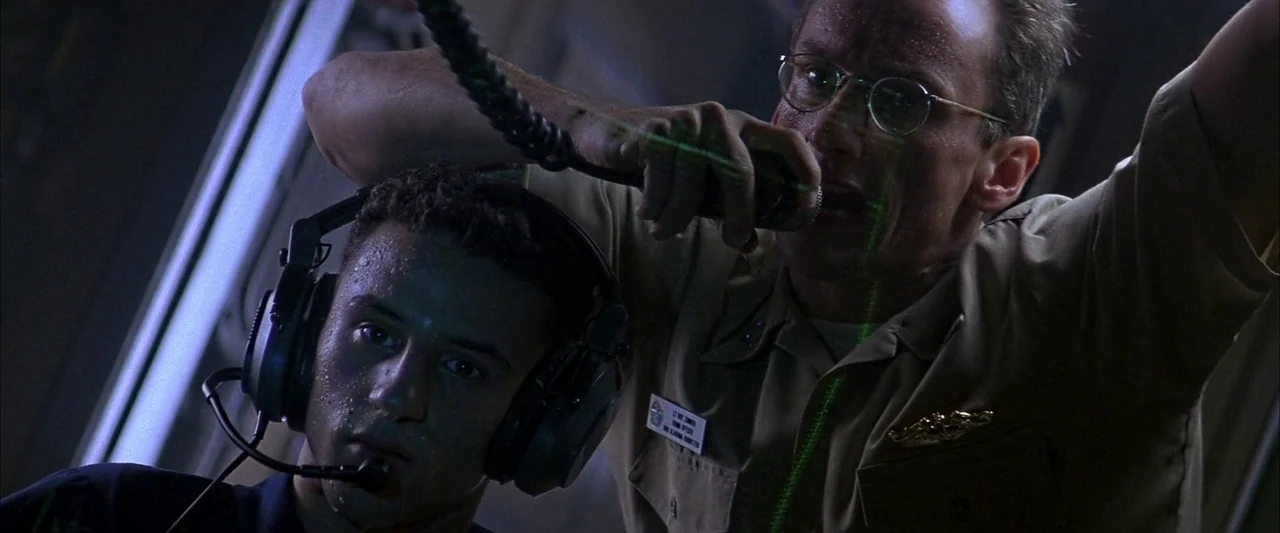 Crimson Tide (1995) movie still: medium — The cramped, metal-walled interior of a submarine is filled with shadows and industrial equipment. An…