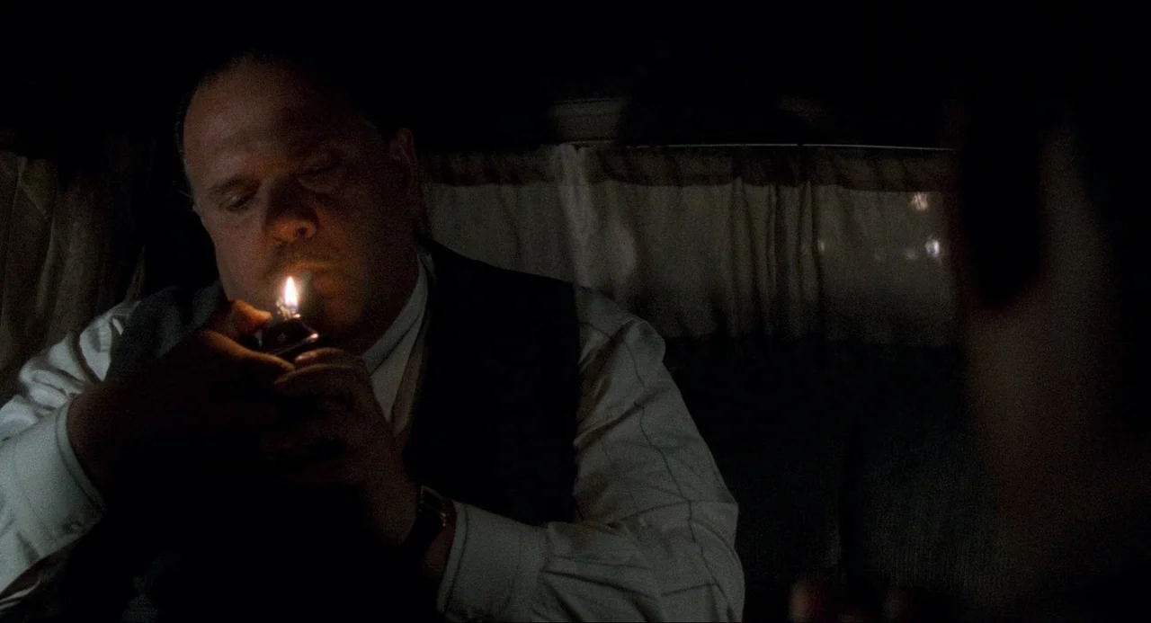 Devil In A Blue Dress (1995) movie still: medium — A man sits inside a dark vehicle illuminated by a flickering flame. He holds a metal lighter near…