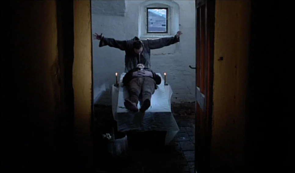 Heart of Glass (1976) movie still: medium — A stone cell with white walls contains a table covered in a white cloth. A man stands behind the table…
