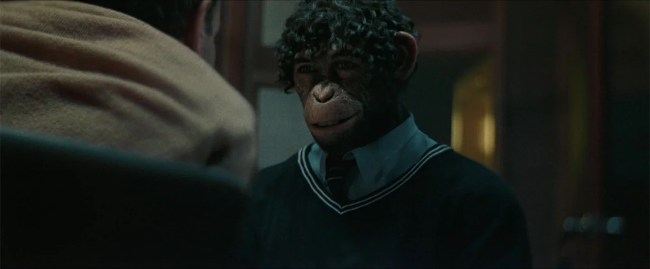 Better Man (2024) movie still: medium — An interior space with dim, low-key lighting and a muted, cool color palette. A chimpanzee dressed in formal…