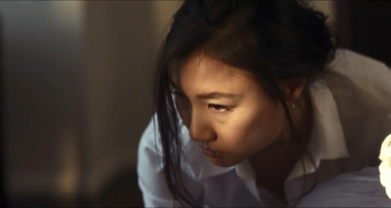 Five Blind Dates (2024) movie still: closeup — A dimly lit indoor space with neutral walls and soft warm light. An east Asian woman in a white shirt…