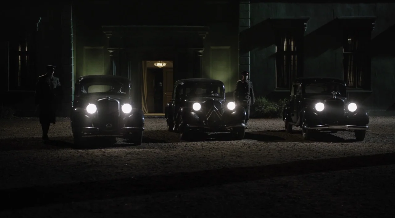 The Death of Stalin (2017) movie still: wide — A dark manor exterior features three vintage black cars idling on a gravel driveway. Two uniformed…