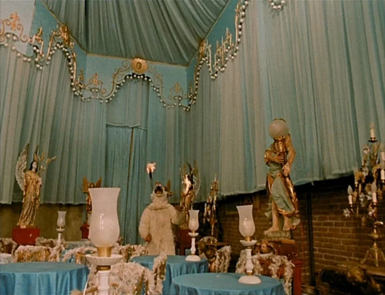 Zazie Dans Le Métro (1960) movie still: wide — A high-ceilinged room features turquoise draped walls and gold-painted wooden angel statues on…