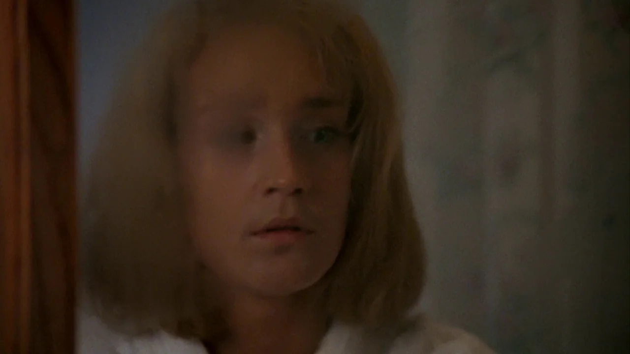 Jason Goes To Hell (1993) movie still: closeup — A dimly lit room interior features a person partially obscured by shadow. A woman with blonde hair…