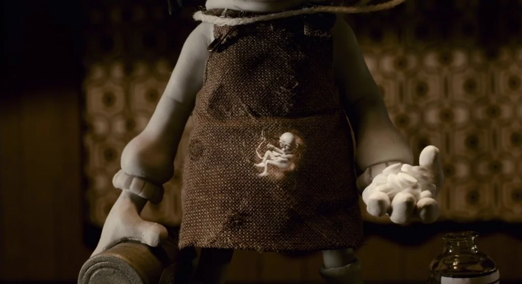 Mary & Max (2009) movie still: medium — A dark, dimly lit space features a grey-skinned puppet wearing a coarse brown apron. The puppet holds a…