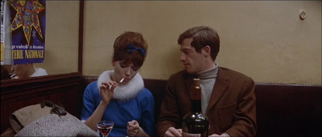 Une Femme Est Une Femme (A Woman Is a Woman) (1961) movie still: medium — Two individuals sit in a booth at a dim establishment with beige paneled…