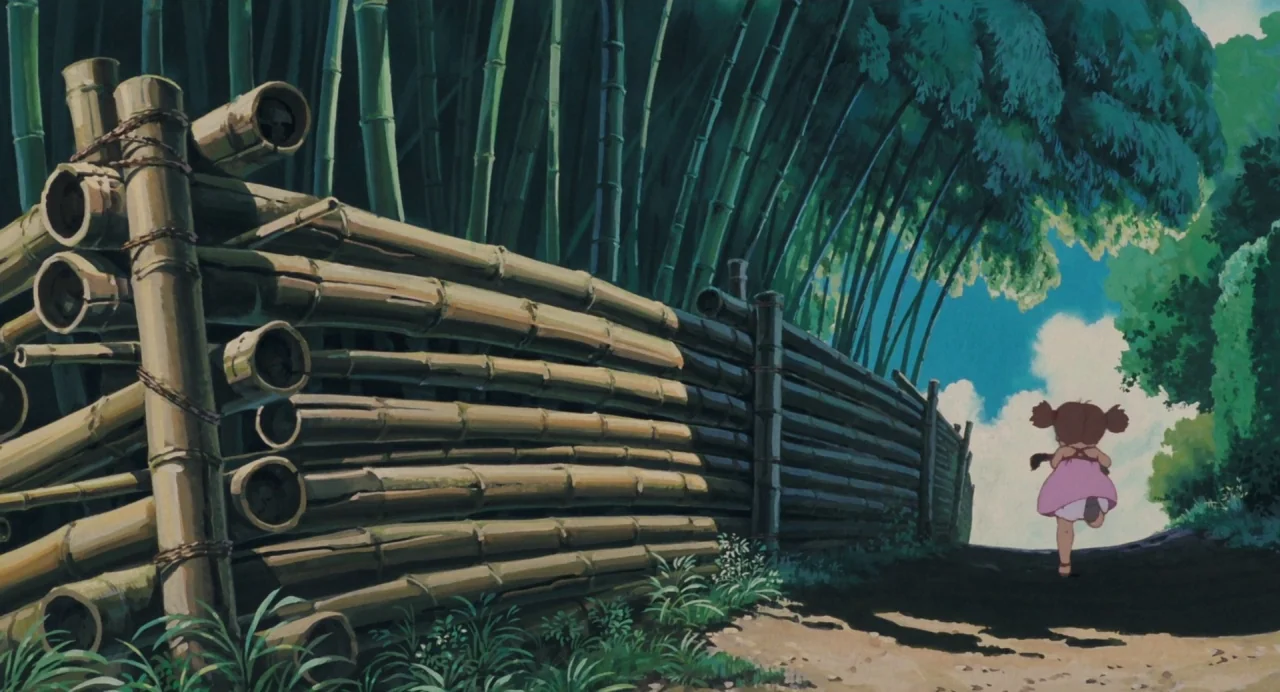 My Neighbour Totoro (1988) movie still: wide — A path bordered by a large, horizontal stack of bamboo logs and tall bamboo stalks. A young child in…