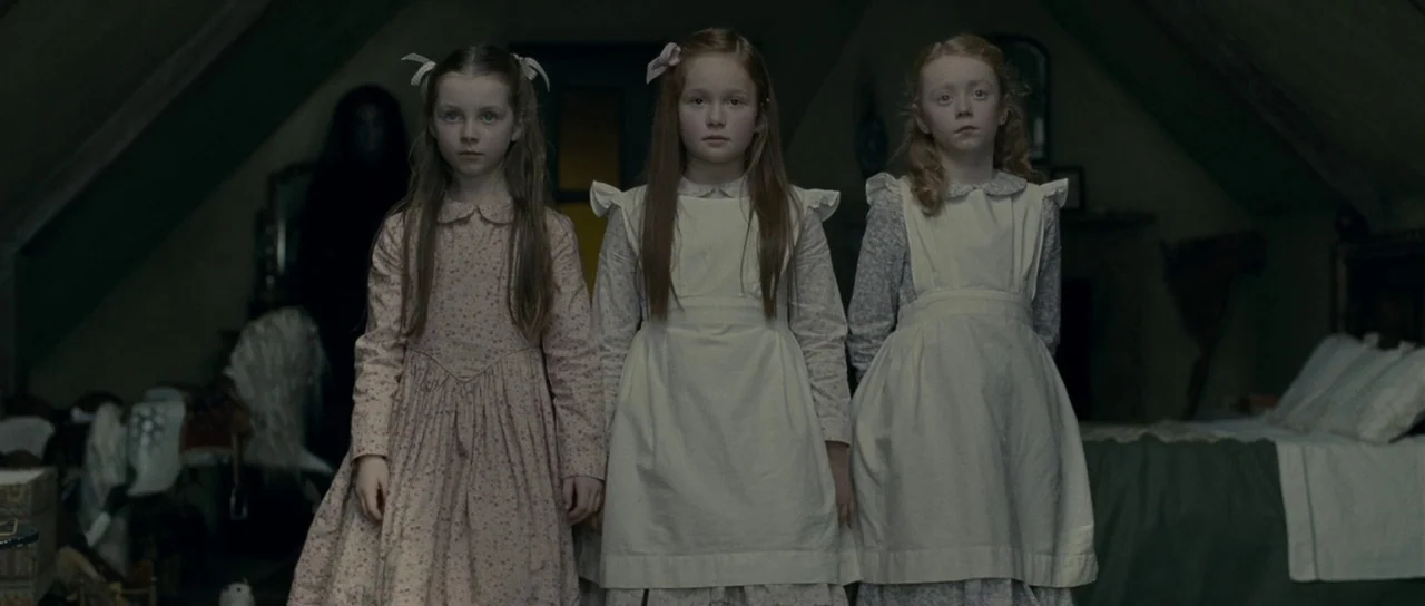 The Woman in Black (2012) movie still: medium — An attic with angled wooden ceilings contains three young girls standing in a row. A dark, obscured…