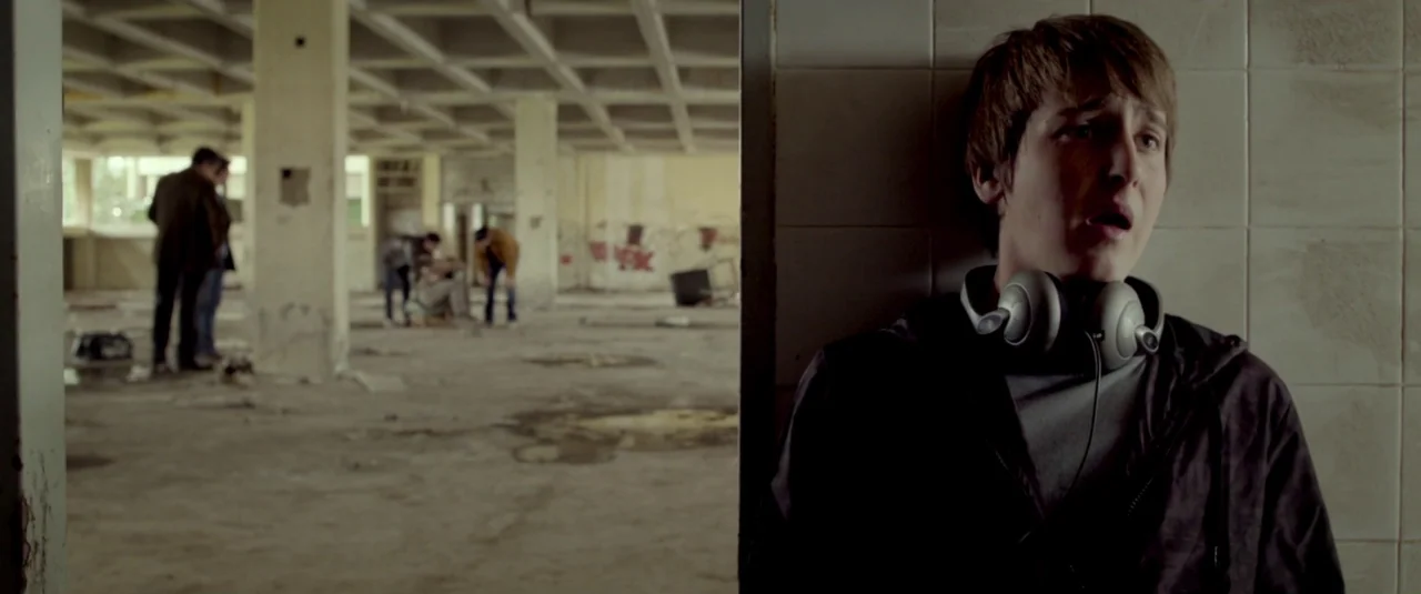 Big Bad Wolves (2013) movie still: medium — A spacious, dusty room with exposed concrete columns and white-tiled wall sections. A young man with…