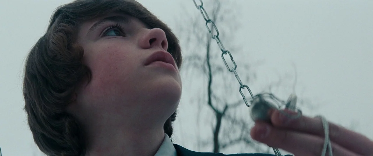 Super 8 (2011) movie still: closeup — An overcast sky serves as a blank backdrop behind a young person outdoors. The youth holds a pocket watch…