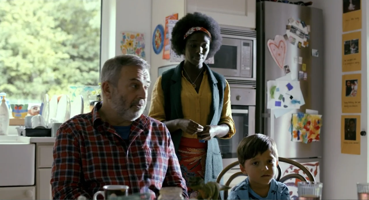 Living Out Loud (1998) movie still: medium — A residential kitchen features white cabinetry and a refrigerator covered in children's artwork. An…
