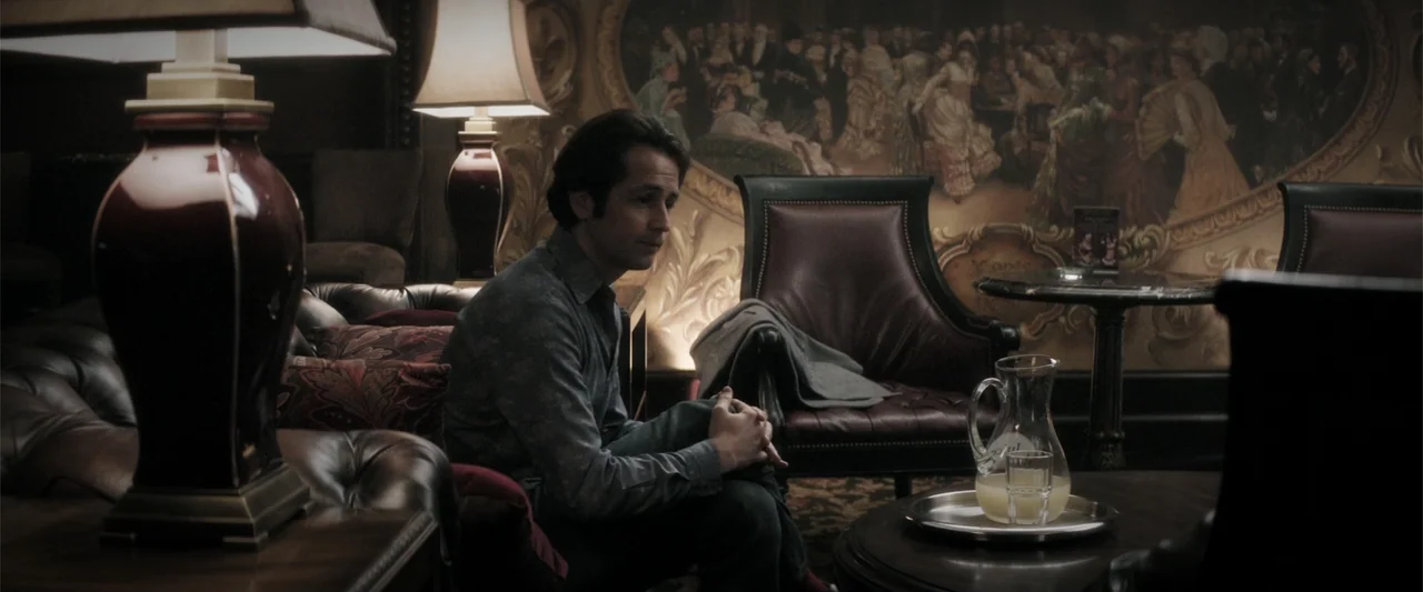 Wild Card (2015) movie still: medium — A dimly lit lounge contains leather chairs and a large ornate wall mural. A man sits alone on a sofa in front…