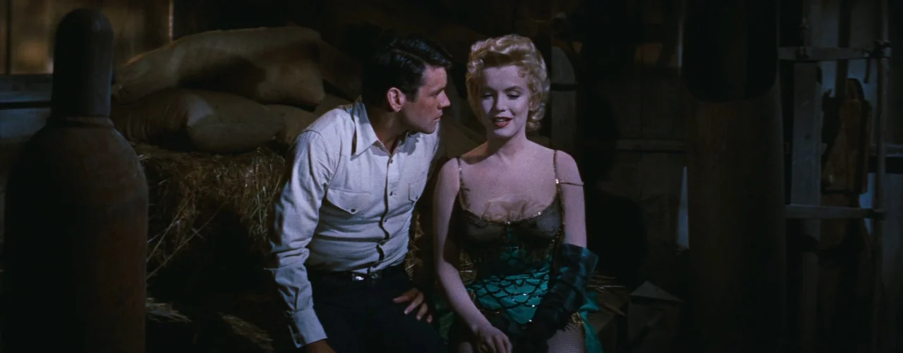 Bus Stop (1956) movie still: medium — A dark wooden barn interior contains hay bales and heavy industrial equipment. A man and a woman in stage…
