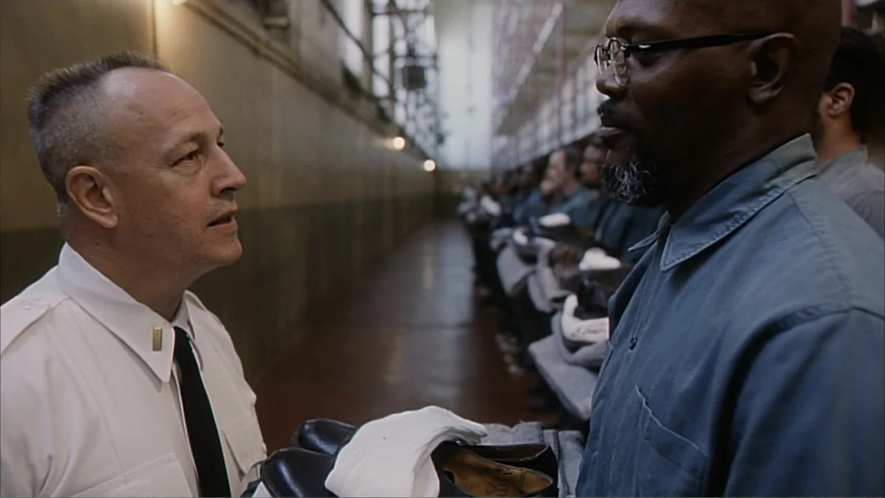 Against the Wall (1994) movie still: medium — A long prison corridor features rows of seated inmates in the background. A guard stands opposite an…
