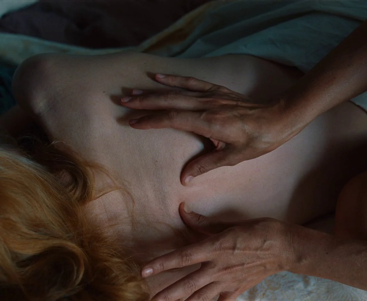 Monica (2022) movie still: closeup — A close view of a person lying on their stomach on a bed. Two hands are massaging the individual's bare upper…