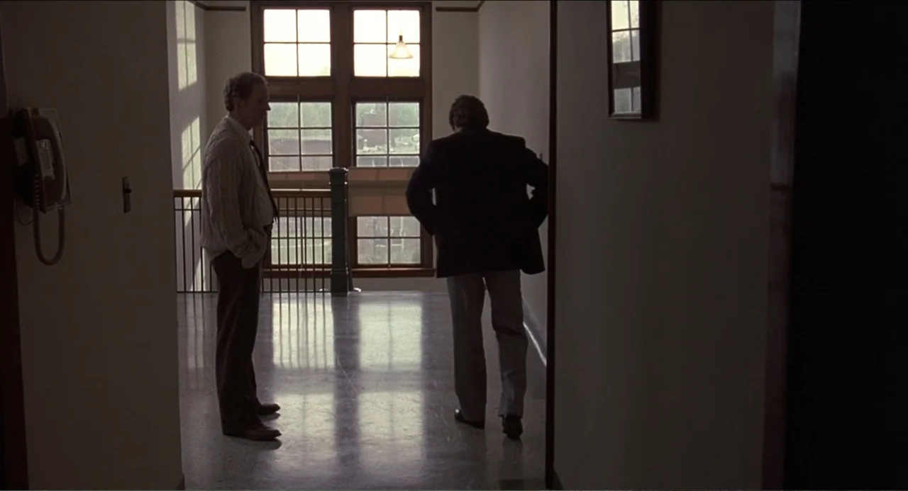 Rain Man (1988) movie still: fullbody — An interior hallway features a large window, tiled flooring, and a wall-mounted telephone. Two men stand in…