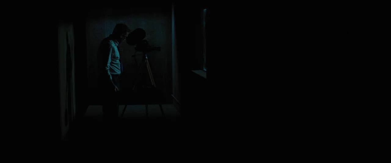 Bad Times at the El Royale (2018) movie still: medium — A dark projection booth features a man standing beside a vintage movie projector. Blue…
