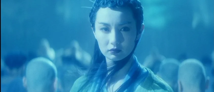 Green Snake (1993) movie still: medium — A woman stands in a crowd of bald-headed figures bathed in monochrome blue light. She stares forward while…