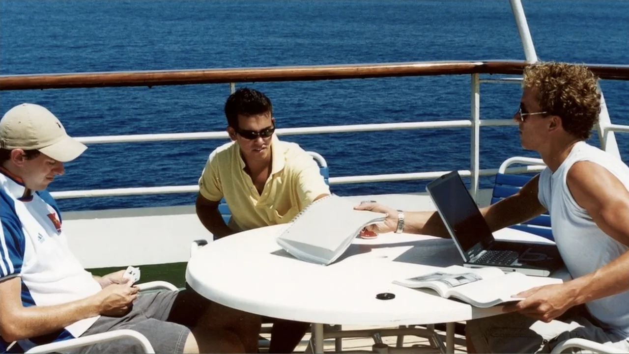 The (Dead Mothers) Club (2014) movie still: fullbody — Three young men sit around a white circular table on the deck of a boat. The man in the…