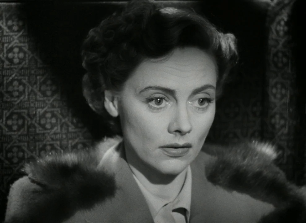 Brief Encounter (1945) movie still: closeup — A woman sits inside a dimly lit train compartment with ornate dark patterned upholstery. The subject…