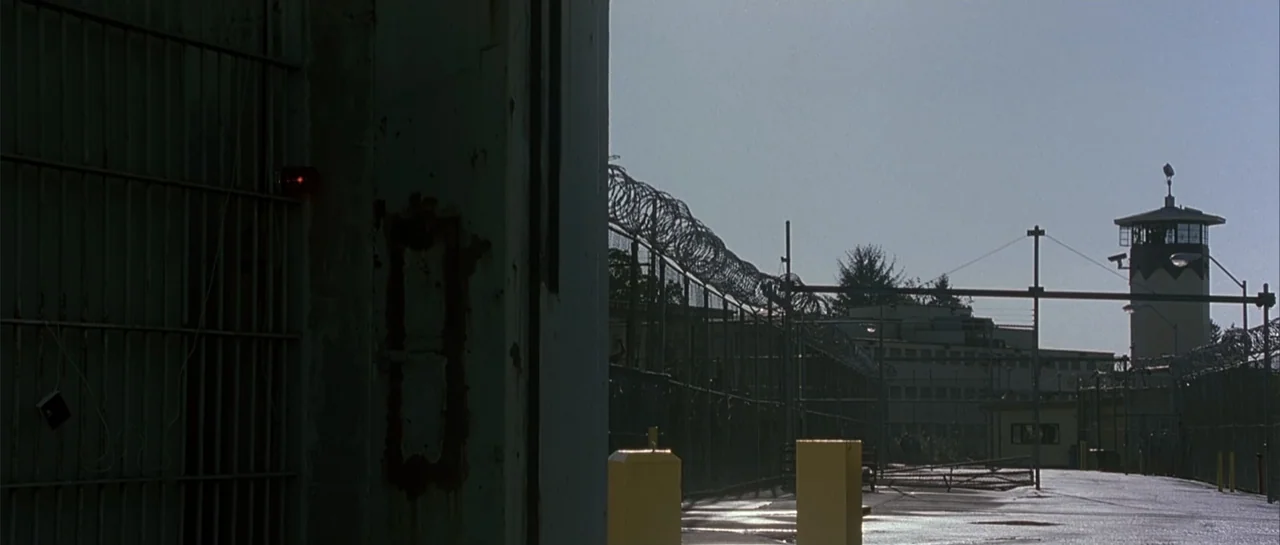 Bandits (2001) movie still: establishing — A secured prison facility features high fences topped with coiled barbed wire and guard towers. The…