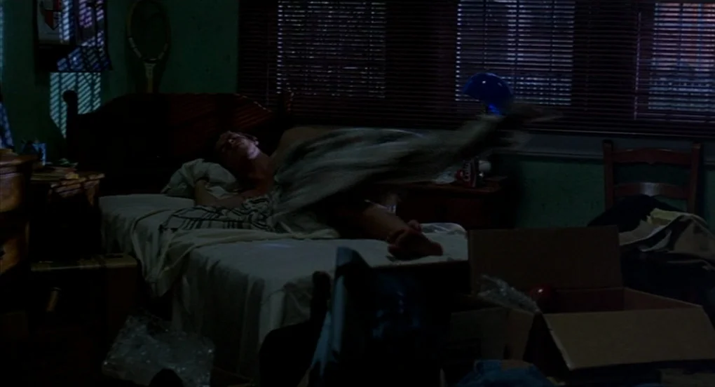 A Nightmare On Elm Street 2: Freddy’s Revenge (1985) movie still: medium — A dimly lit room with green walls and various cardboard boxes scattered…