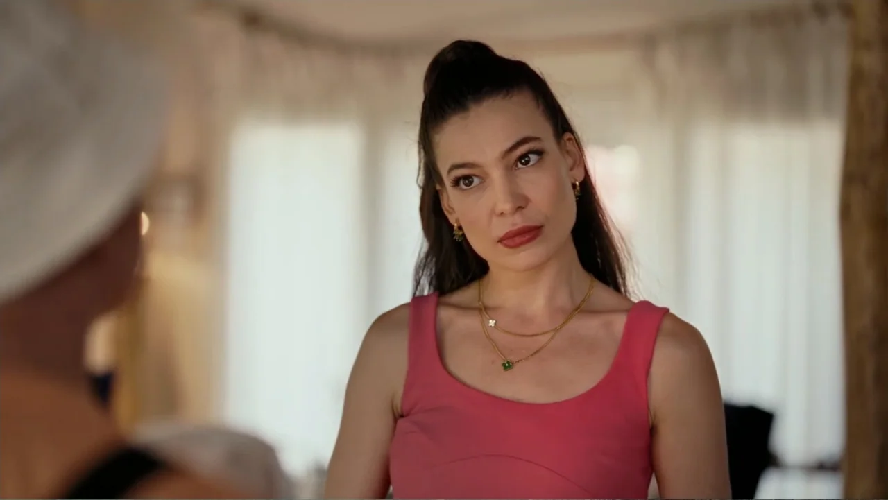 Paranormal Cuma (2024) movie still: medium — An interior living room with sheer curtains visible in the blurred background. A woman in a pink top…