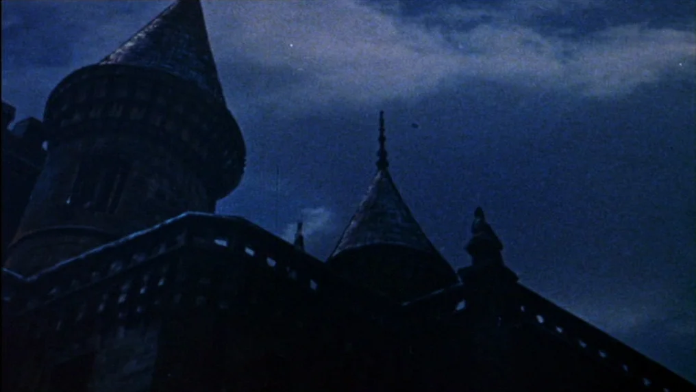 Targets (1968) movie still: establishing — A gothic stone castle silhouette rises against a cloudy, deep blue night sky. The tall towers and pointed…