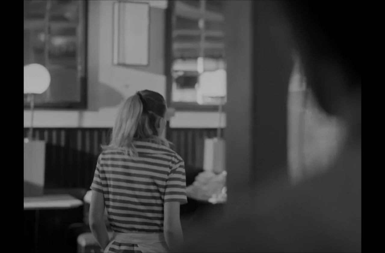 The Kitchen (2012) movie still: medium — A dimly lit room features a server moving through a blurred commercial space. The focus remains on the back…