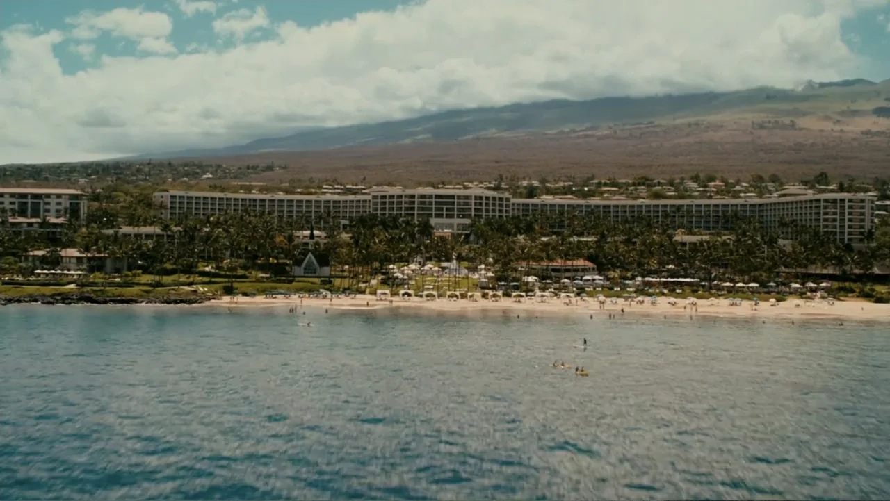 Just Go with It (2011) movie still: establishing — A wide coastal landscape shows a large hotel complex bordering a sandy beach. The blue ocean…