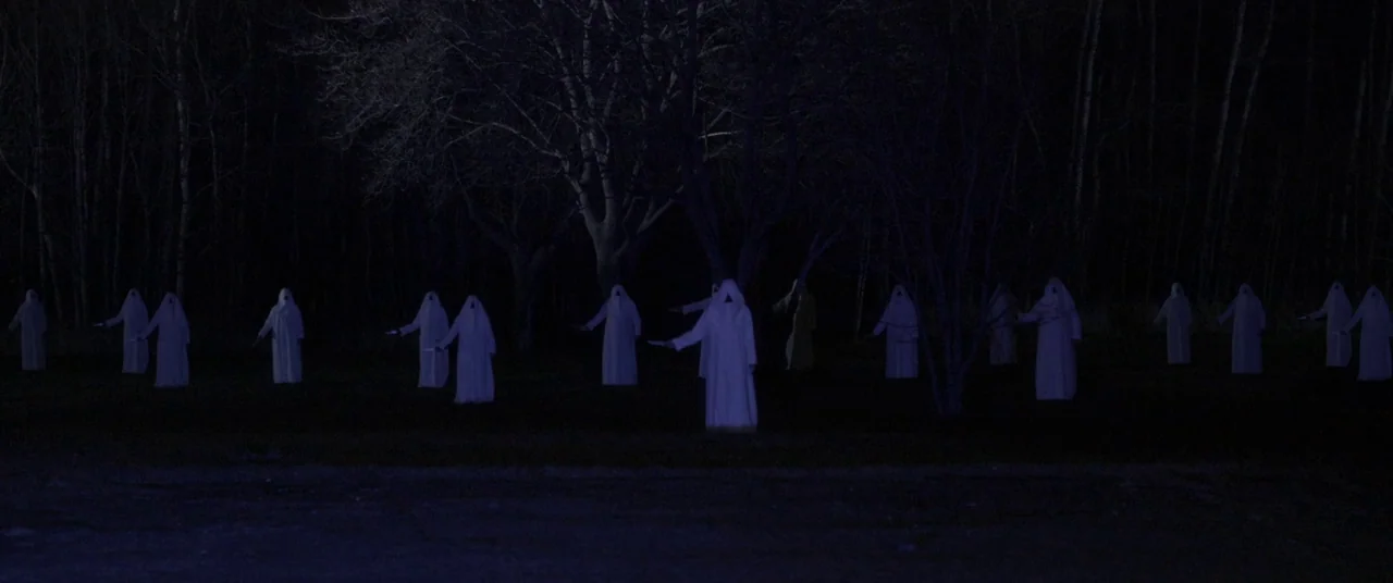 The Void (2016) movie still: wide — A group of figures in white robes stands across an open dark field. The individuals hold blades outstretched…