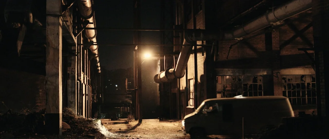 The Possession (1950) movie still: wide — A narrow alleyway between old brick industrial buildings at night is lit by a streetlamp. A white cargo…