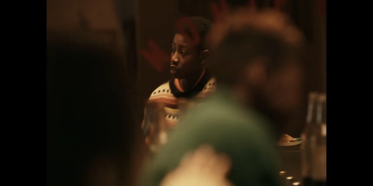 Autumn Beat (2022) movie still: medium — A dimly lit interior with soft warm lighting and blurred foreground elements. A person wearing a striped…