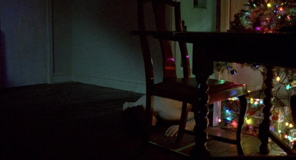 Morvern Callar (2002) movie still: medium — A dark, sparsely furnished room contains a dining chair near a decorated Christmas tree. A person lies…