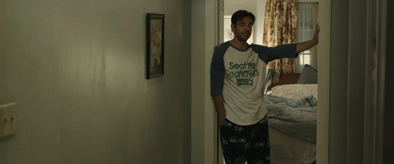 Overboard (2018) movie still: medium — A residential bedroom doorway features an interior hallway wall with a small framed picture. A man in…